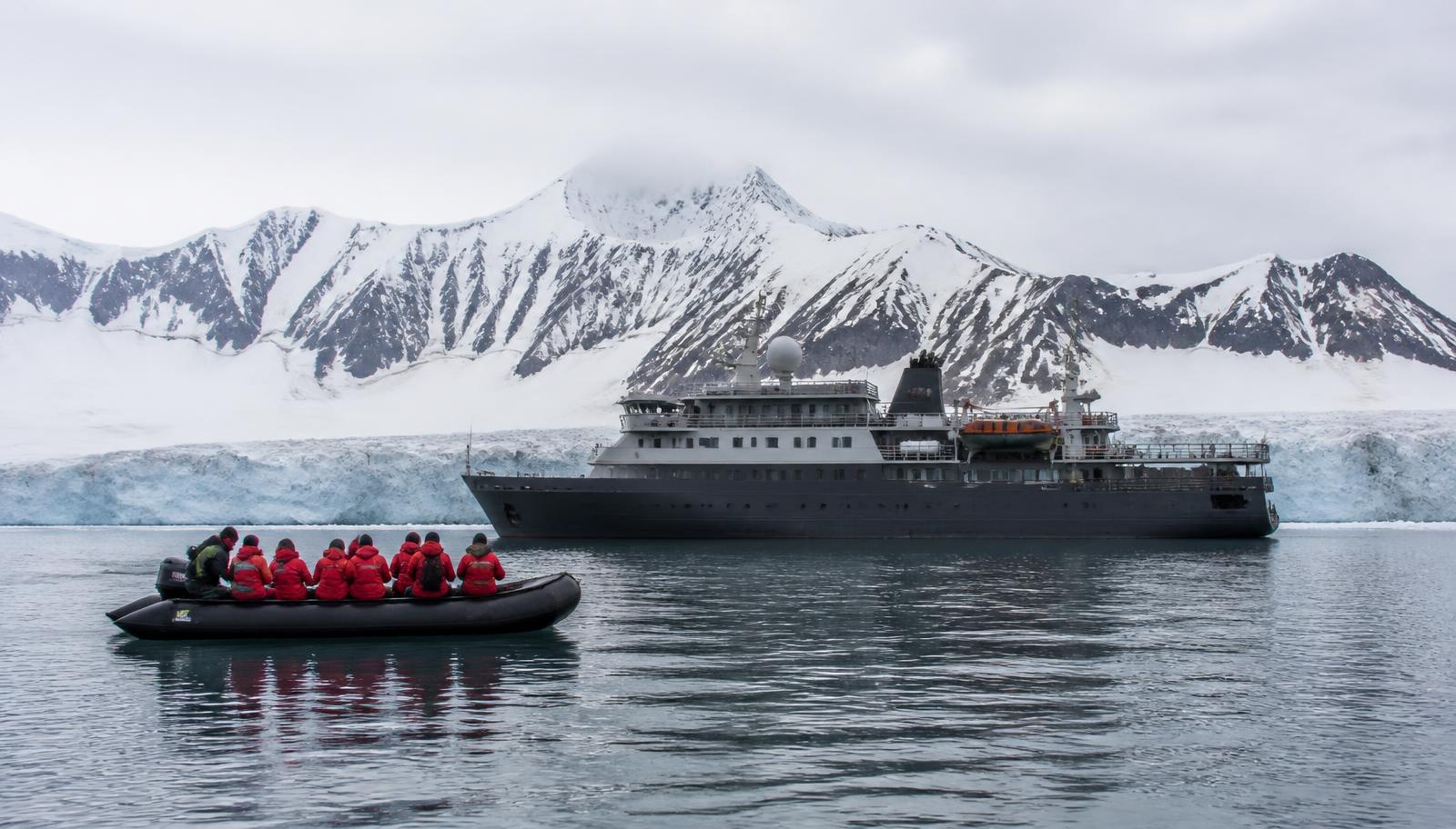Navire d'expédition au mouillage devant des montagnes enneigées, zodiac en approche